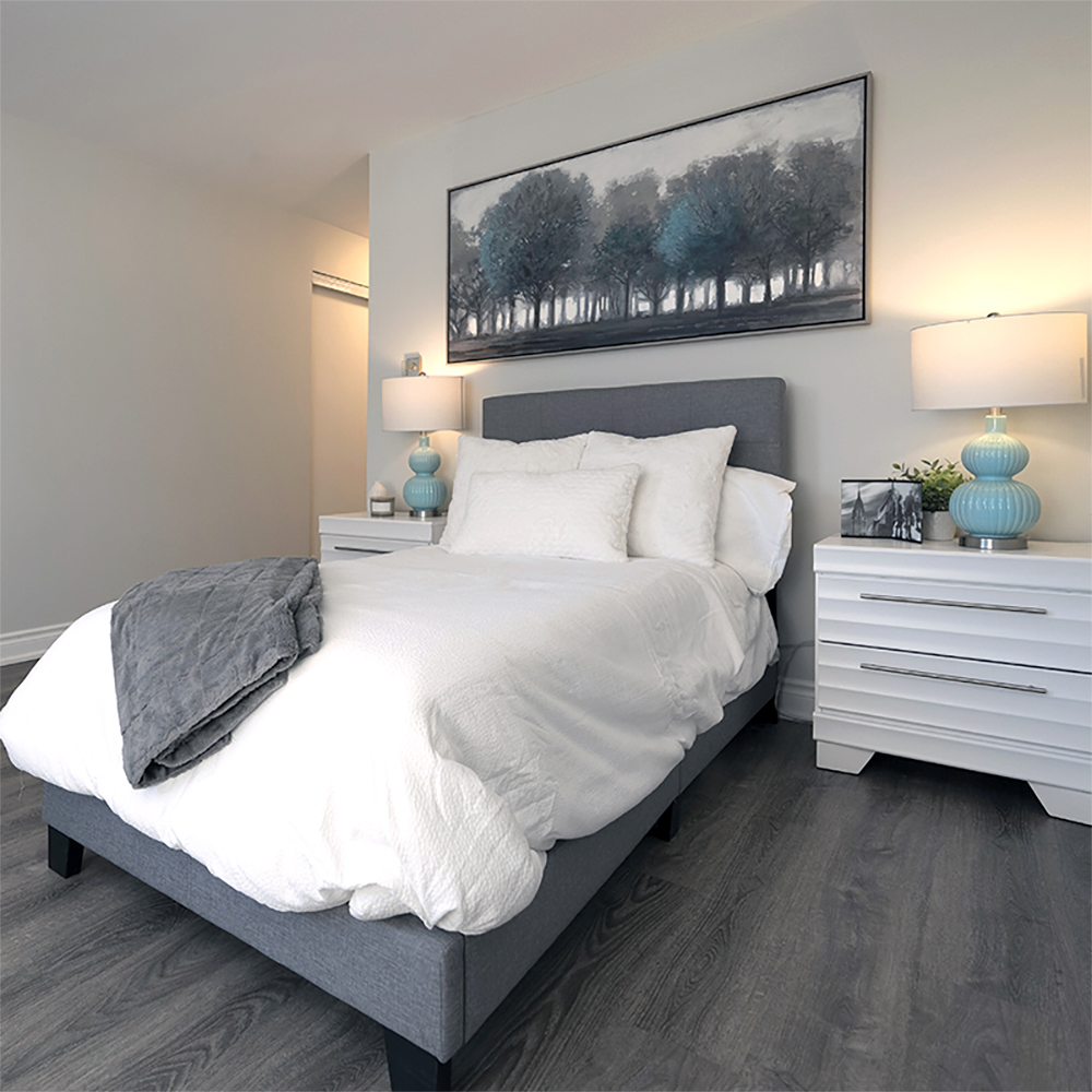 A single bed in a cosy and welcoming bedroom suite flanked by night white night stands and stylish lamps at ATrium Retirement Residence